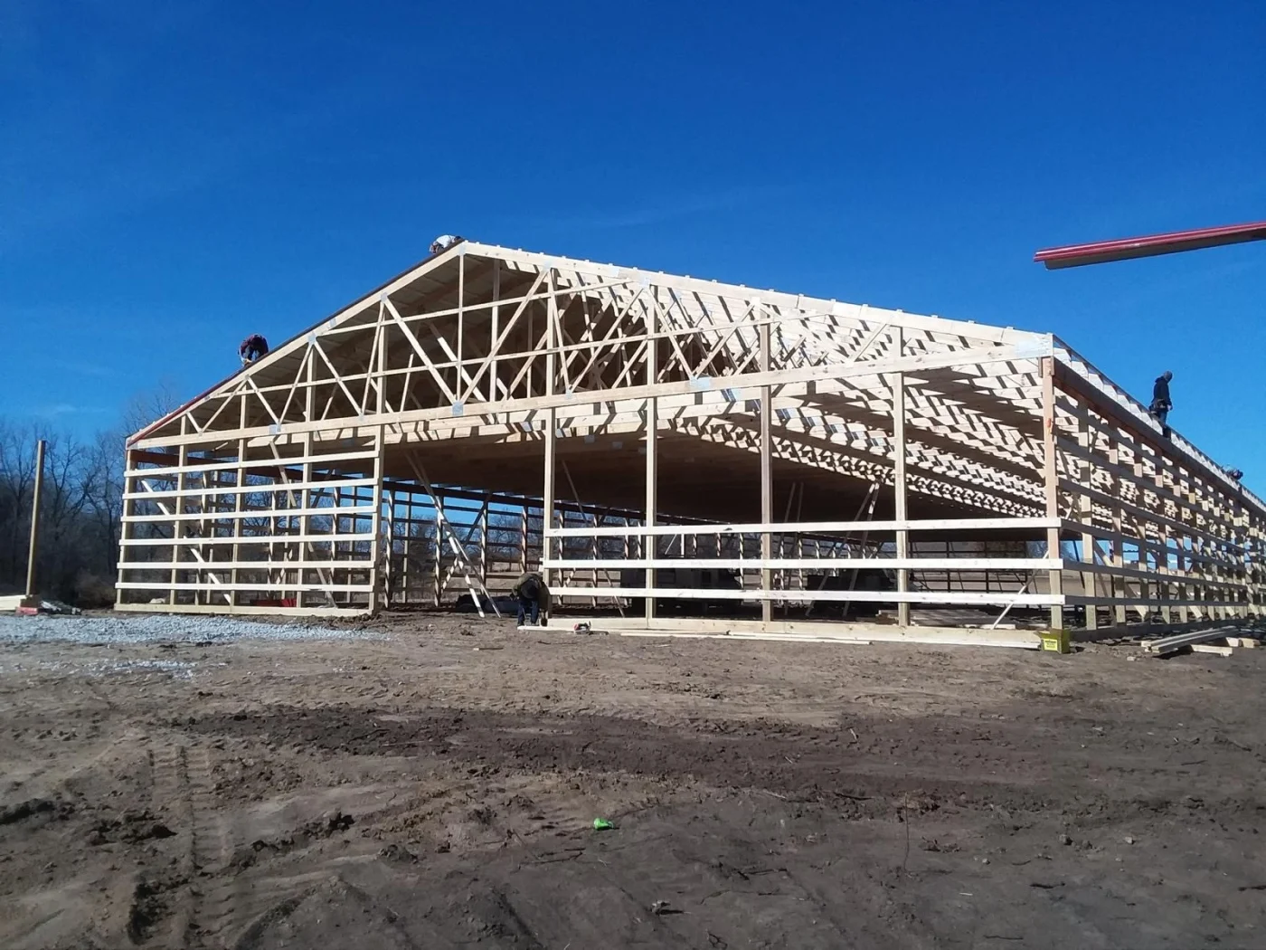 Dependable Residential Truss | Liberty, MO | North Country Truss A large wooden truss building frame under construction on a muddy job site, with workers on the roof structure and a clear blue sky overhead.