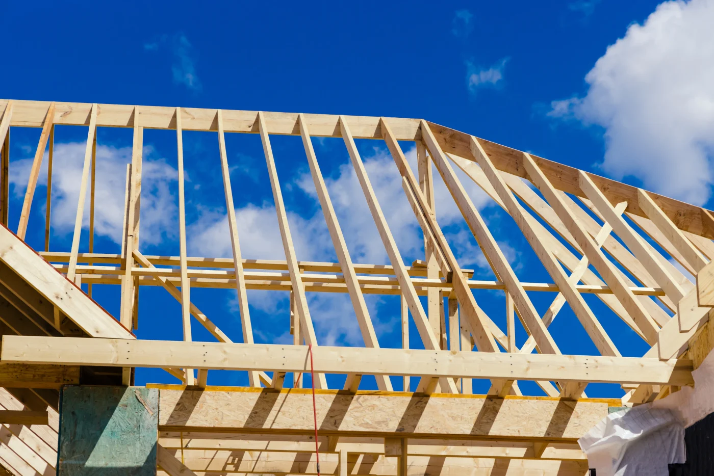 A close-up view of the exposed beams of a roof that’s under construction. The support structure is visible, with blue sky showing between the beams and trusses.