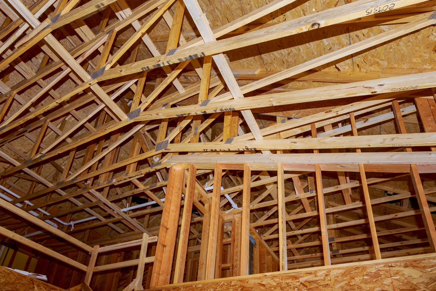 A photo taken from the floor and looking up at the wooden framing and truss positions beneath the roof of a building with a high, wide ceiling. There are multiple levels and sections of this building, each supported by a different arrangement of beams and boards.