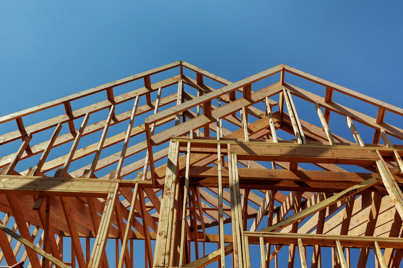 Great Barndominium Truss In Warrensburg, MO | North Country Truss A photo looking up at part of the wooden framing of a home under construction. There are multiple sections of roof and supports visible; some are narrow, others have a wider span.